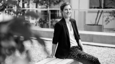Elena Hassinger sitzt im Freien und lächelt in die Kamera, professionelles Porträtfoto für Pressezwecke.